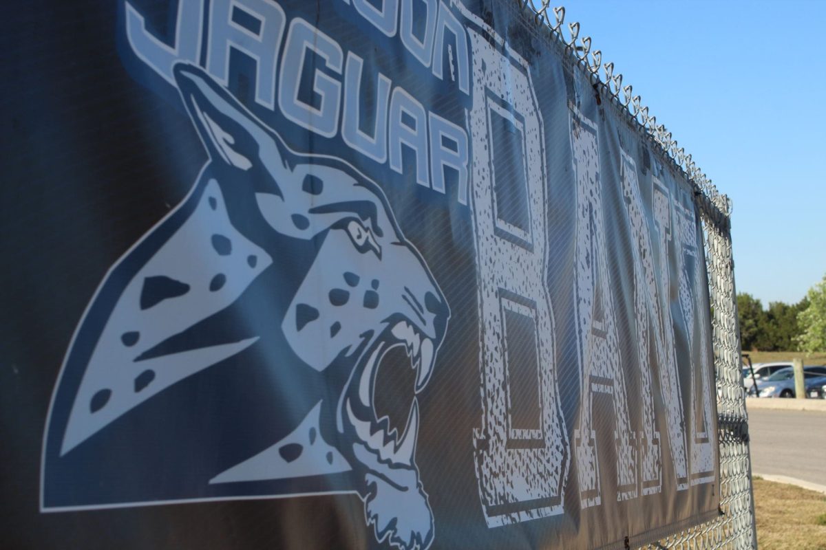 The Johnson Jaguar Band banner hanging on the fence by the band pad. It is in school colors and depicts the school mascot. The picture is taken from a side angle.