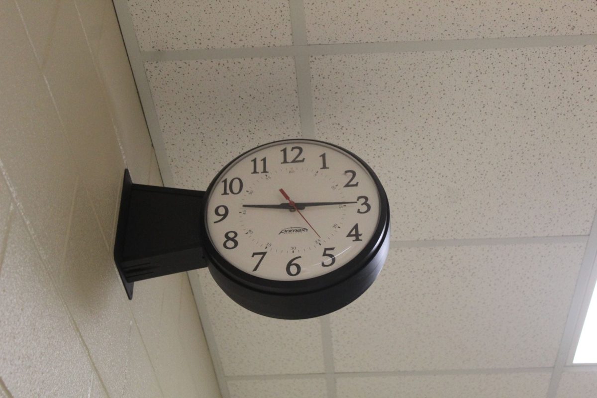 An analog clock is suspended next to a beige cinderblock hallway wall.