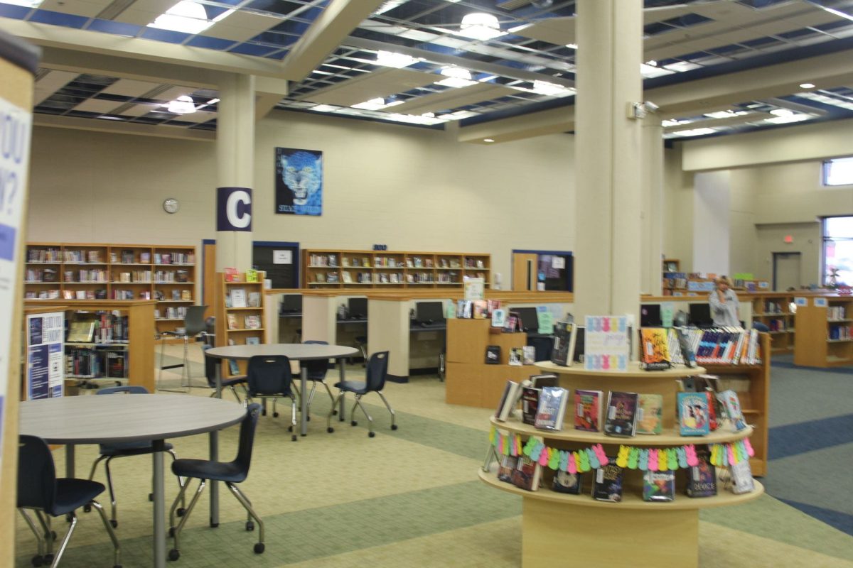 The school library is shown in a pano shot, there is a table in the bottom left corner and bookshelves across the back wall.