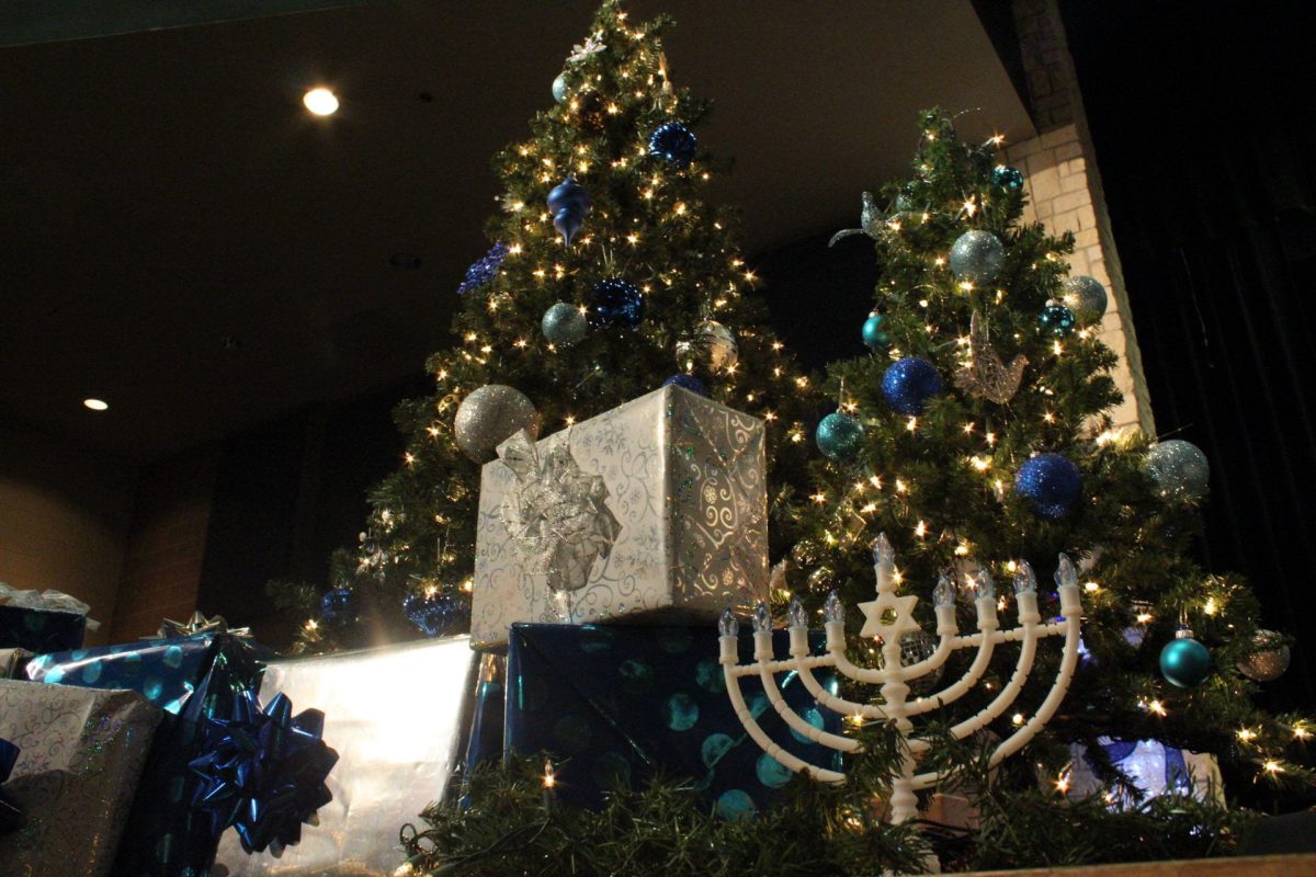 The+winter+decorations+line+the+stage+for+the+band+concert.+There+is+a+lit+up+Christmas+tree%2C+gift+boxes+wrapped+in+festive+papers%2C+and+a+menorah+with+the+Star+of+David+in+the+middle.